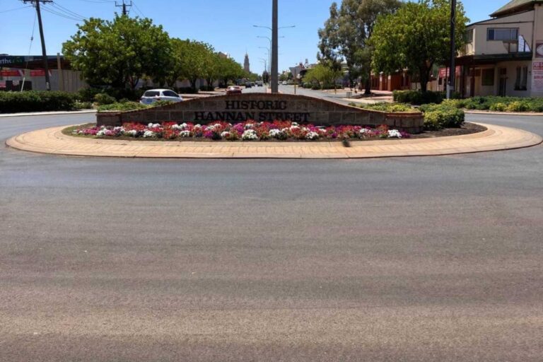 Roundabout on Hannan Street with a landscaped garden bed and a sign reading 'Historic Hannan Street', on a sunny Kalgoorlie Boulder street.
